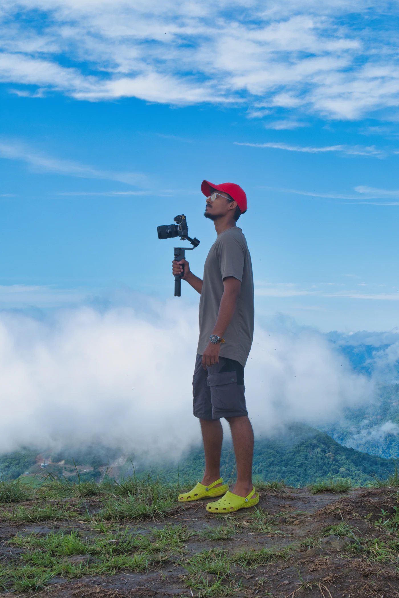 A man holding a camera gimbal on a mountain top above the clouds