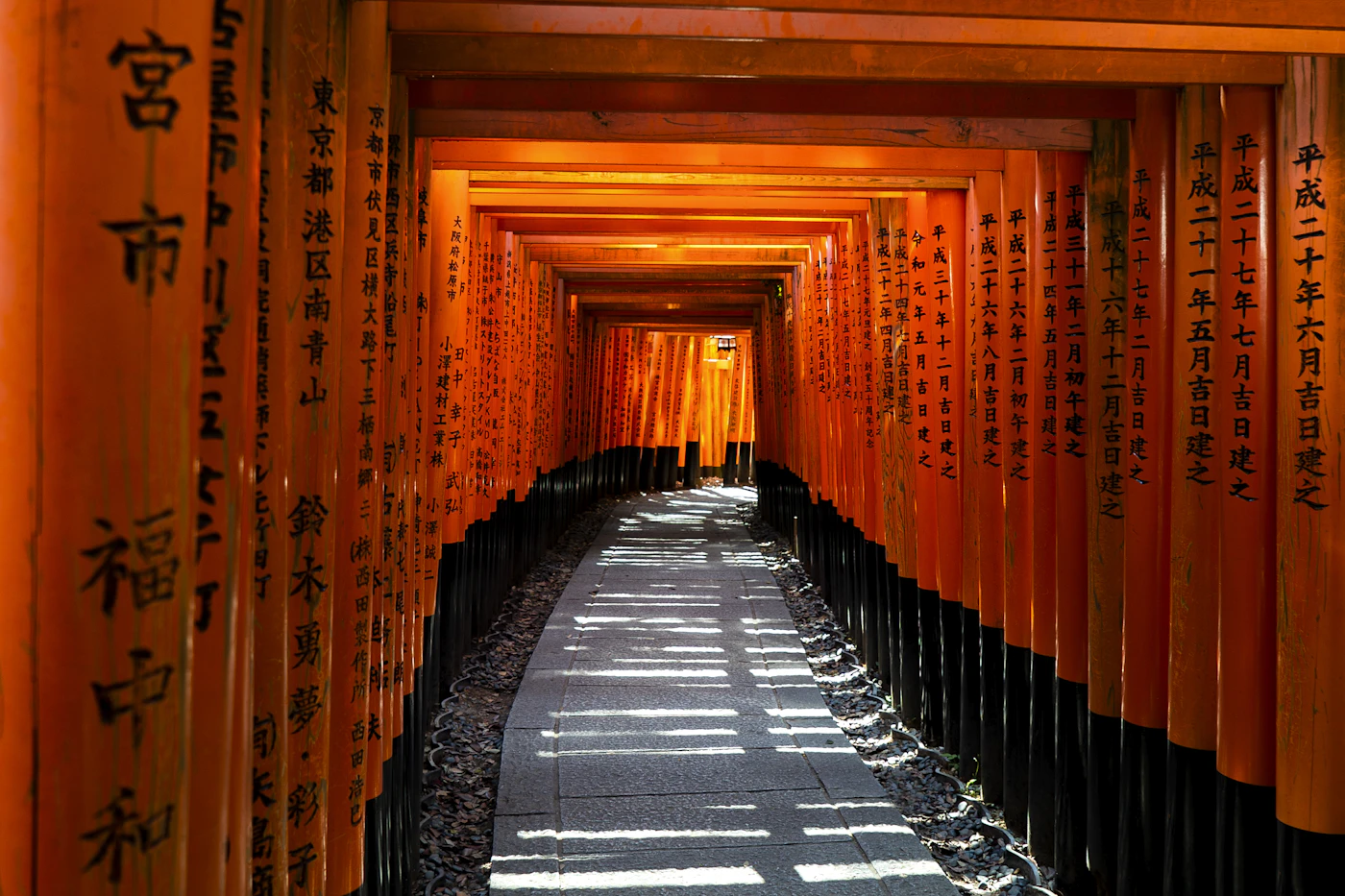 A stone path through a tunnel of orange torii gates in Kyoto